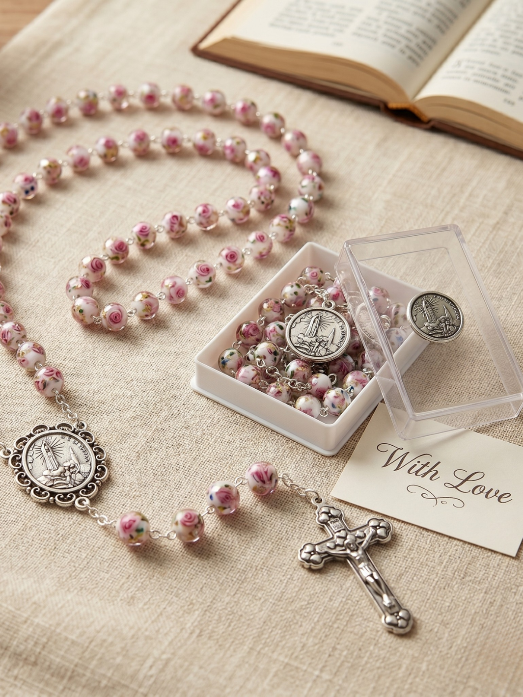 Pink rosary with silver cross and medals on a beige surface with an open book.
