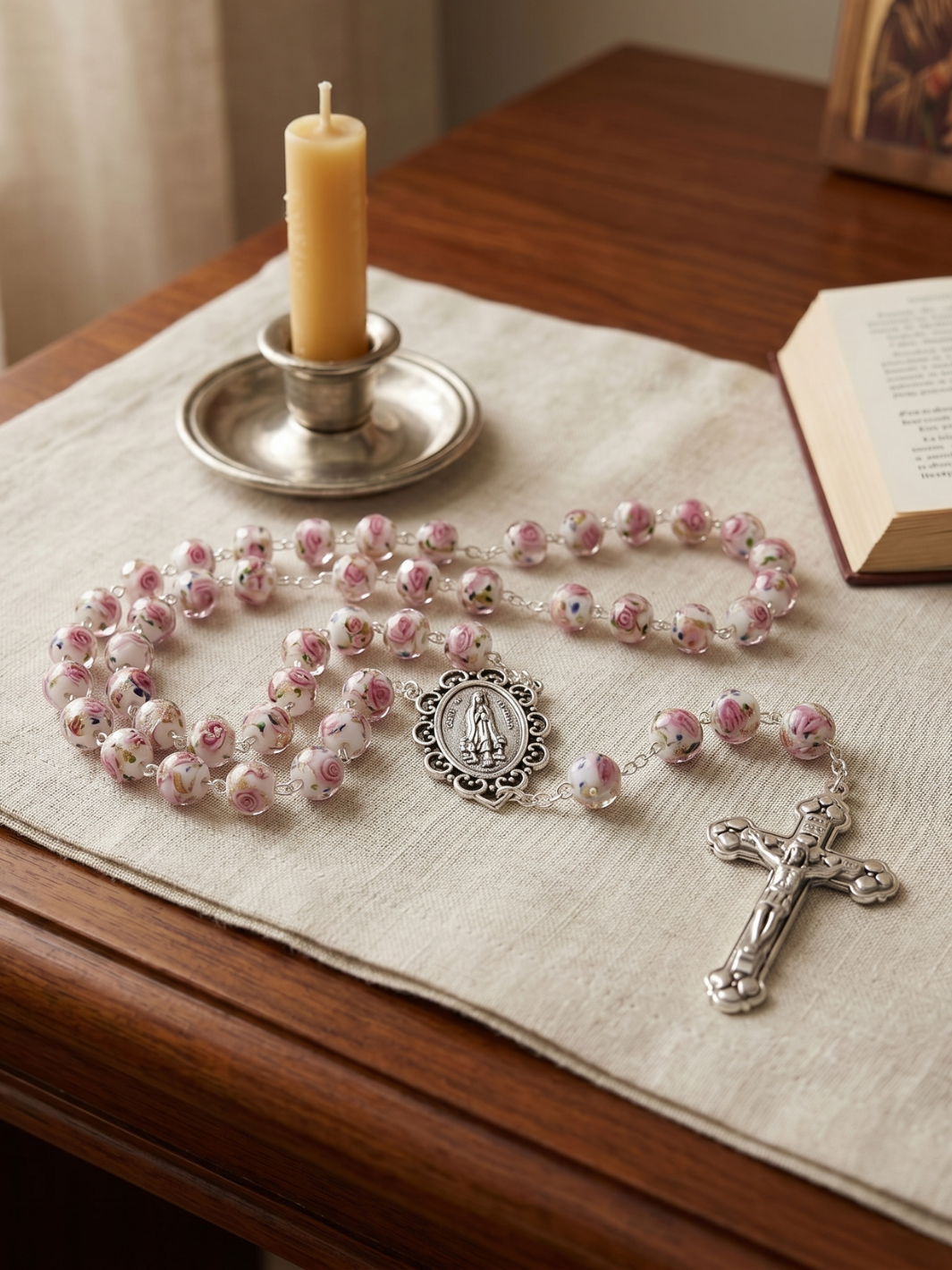 Pink rosary with silver crucifix and medal on a wooden surface with a lit candle