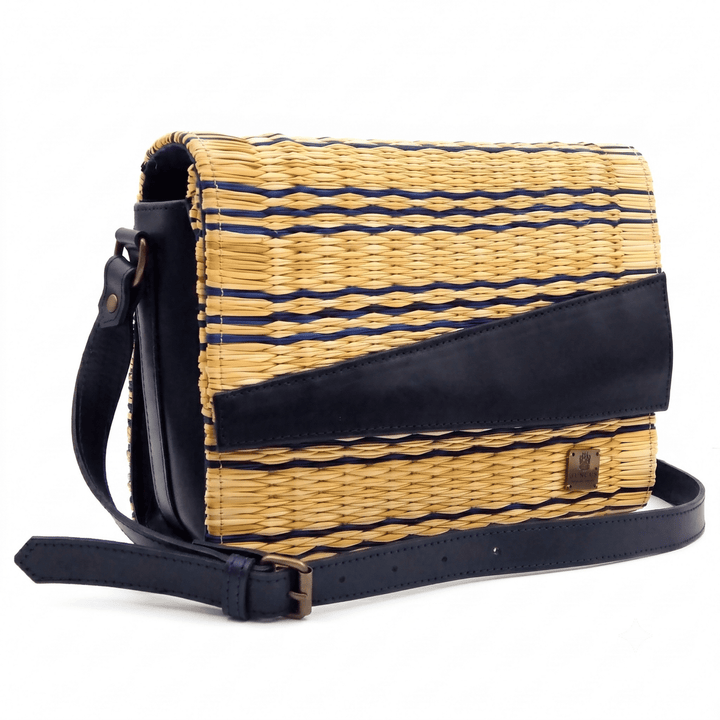 A woven straw crossbody bag with navy blue leather trim and a matching shoulder strap, set against a plain white background.