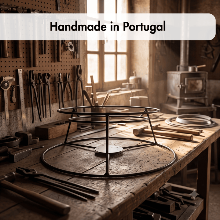 A metal circular stand or rack made from black metal pipes sits on a rustic wooden workbench inside a warm, sunlit workshop. Tools hang on the wall behind it, and a stove is visible in the background.