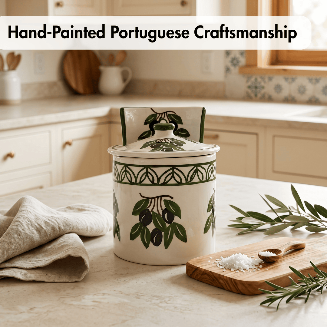 A hand-painted ceramic canister with a lid, decorated with green olive branches and black olives on a cream background, set on a kitchen counter next to a wooden cutting board and olive leaves.