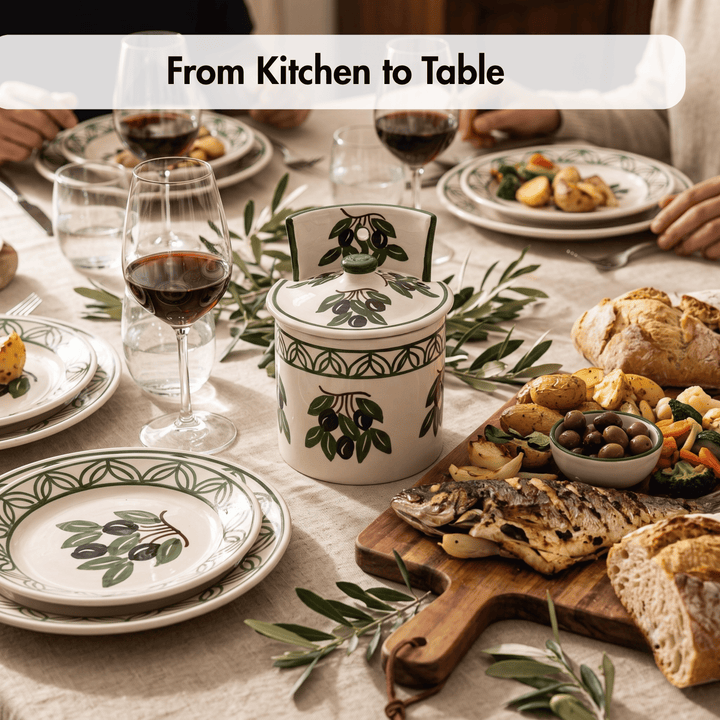 A ceramic lidded jar with olive branch illustrations sits on a dining table set for a meal, surrounded by plates, wine glasses, bread, and a cutting board with grilled fish and olives. A text banner at the top reads &