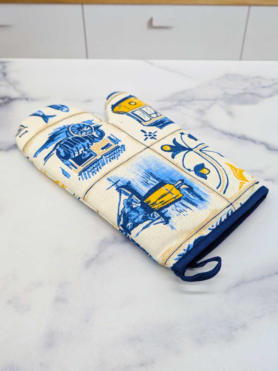 Decorative oven mitt and pot holder with blue and yellow patterns on a marble surface.