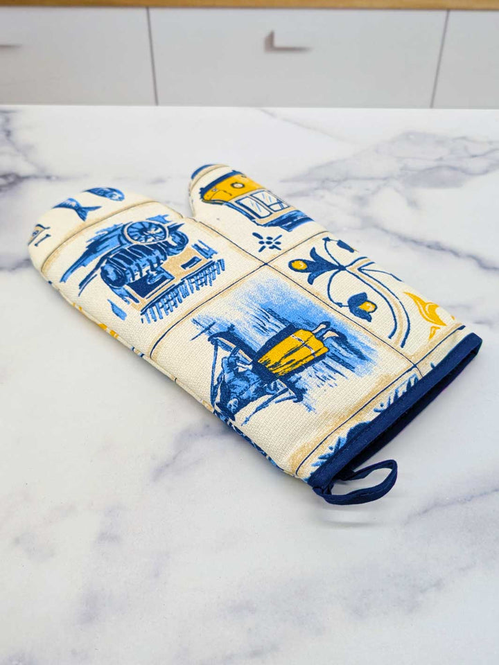 Decorative oven mitt and pot holder with blue and yellow patterns on a marble surface.