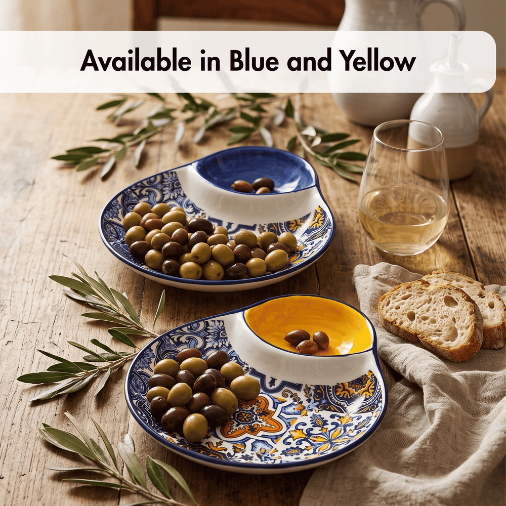 Two decorative serving platters with blue, yellow, and white patterns, shown on a rustic wooden table with olives, bread, olive branches, a glass of white wine, and ceramic pitchers. A text banner at the top reads 'Available in Blue and Yellow'.