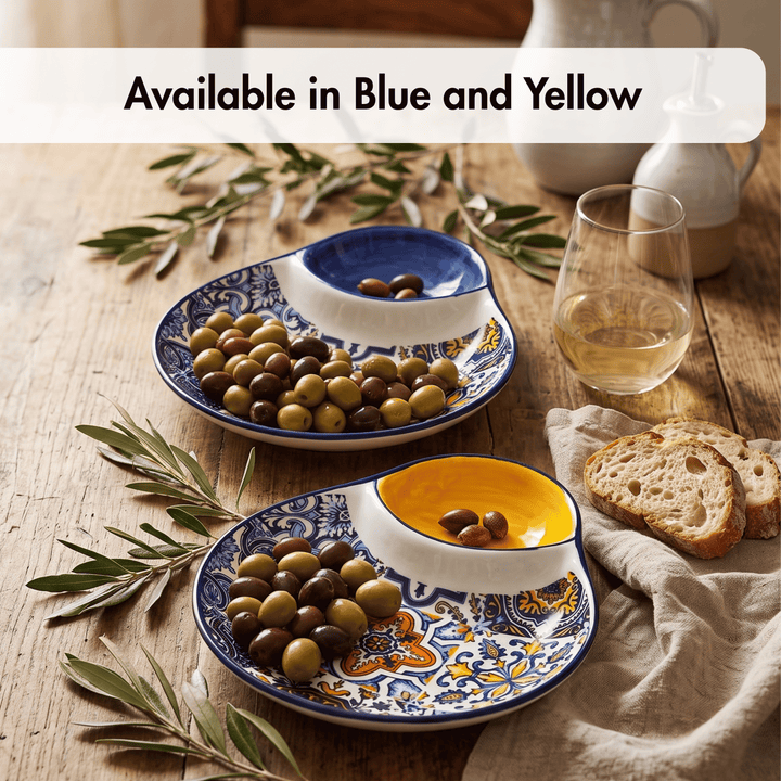 Two decorative serving platters with blue, yellow, and white patterns, shown on a rustic wooden table with olives, bread, olive branches, a glass of white wine, and ceramic pitchers. A text banner at the top reads &