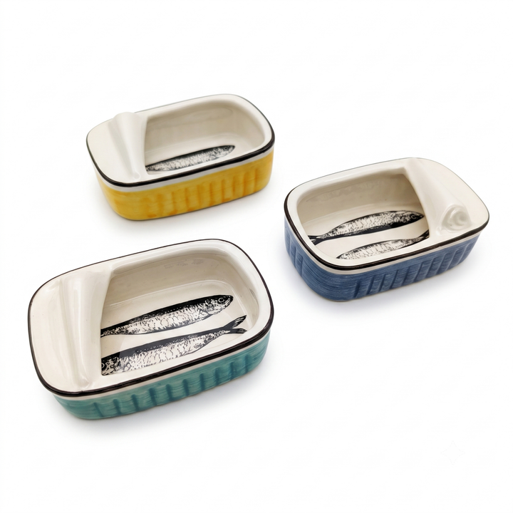 Three small rectangular ceramic dishes with ribbed sides and fish illustrations, shown on a white background. One dish is yellow, one is teal, and one is blue, each with a cream interior and a black rim.