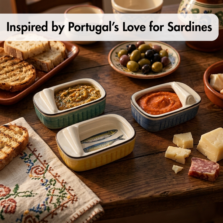 Three small rectangular ceramic sardine cans with lids, shown open on a rustic wooden table with bread, olives, cheese, and cured meat. A text banner at the top reads, &
