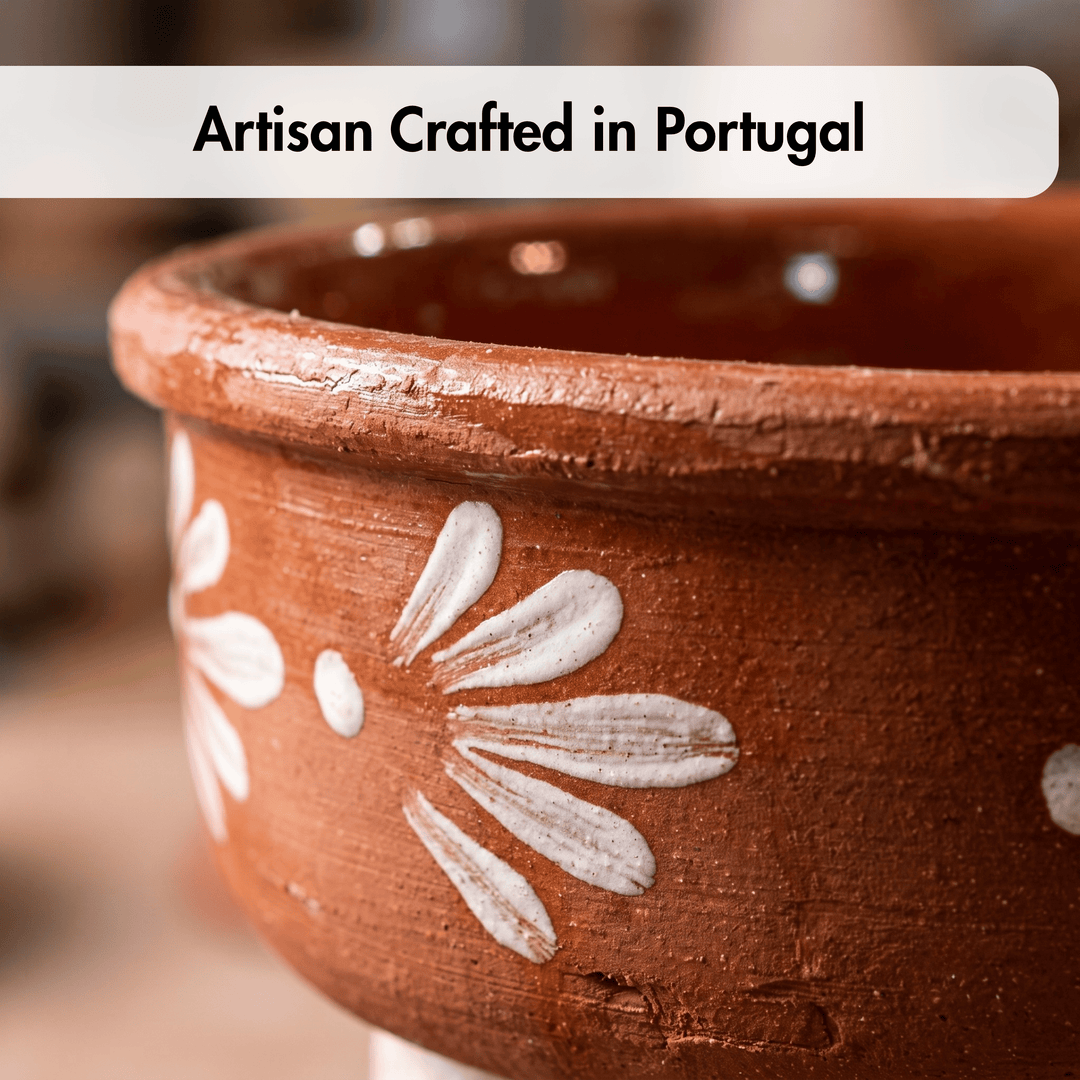Close-up of a handmade terracotta clay pot with white hand-painted floral motifs, featuring a text overlay that reads &