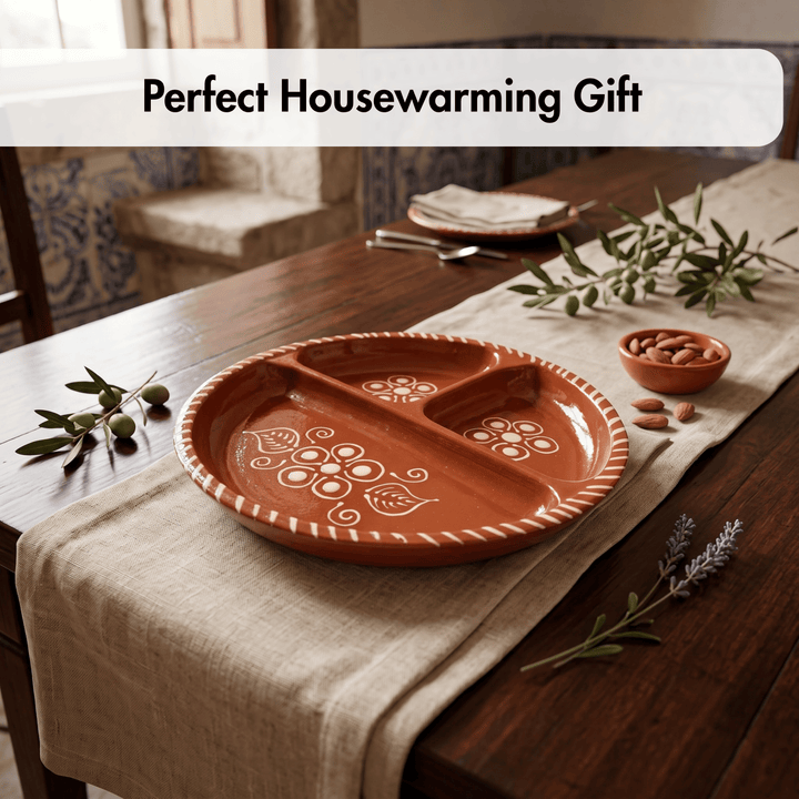 A terracotta-colored ceramic three-compartment divided serving platter with white floral patterns, displayed on a linen table runner on a wooden dining table with olive branches and almonds. A text banner at the top reads &