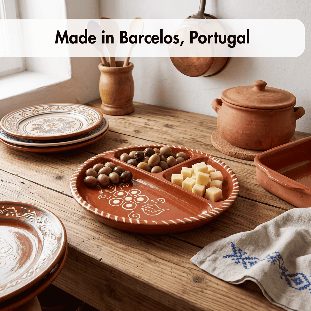 A rustic terracotta clay serving platter with three compartments, styled on a wooden table with olives and cheese cubes. Other matching clay dishes and a lidded pot are visible in a warm, sunlit kitchen setting, with a text overlay reading &