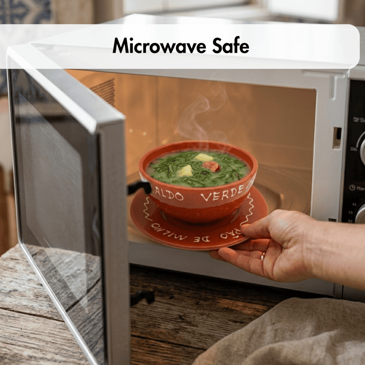 A hand holds a red ceramic bowl and saucer with Spanish text, placing it into a white microwave. Steam rises from the soup inside, and a white banner at the top reads &