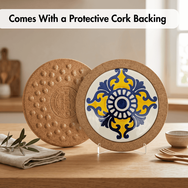 Two round cork coasters displayed on a wooden table. One coaster is shown from the back with a textured cork surface and debossed logo, and the other is shown from the front with a white center, blue and yellow ornamental tile pattern, and a cork border.