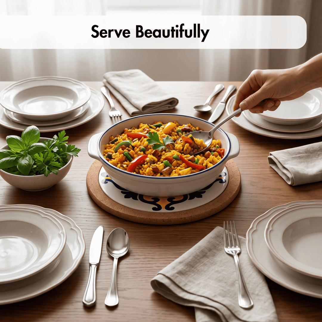 A ceramic serving bowl filled with colorful rice and vegetables sits on a wooden trivet on a dining table, surrounded by plates, napkins, silverware, and a small bowl of fresh herbs. A hand is holding a spoon over the bowl.