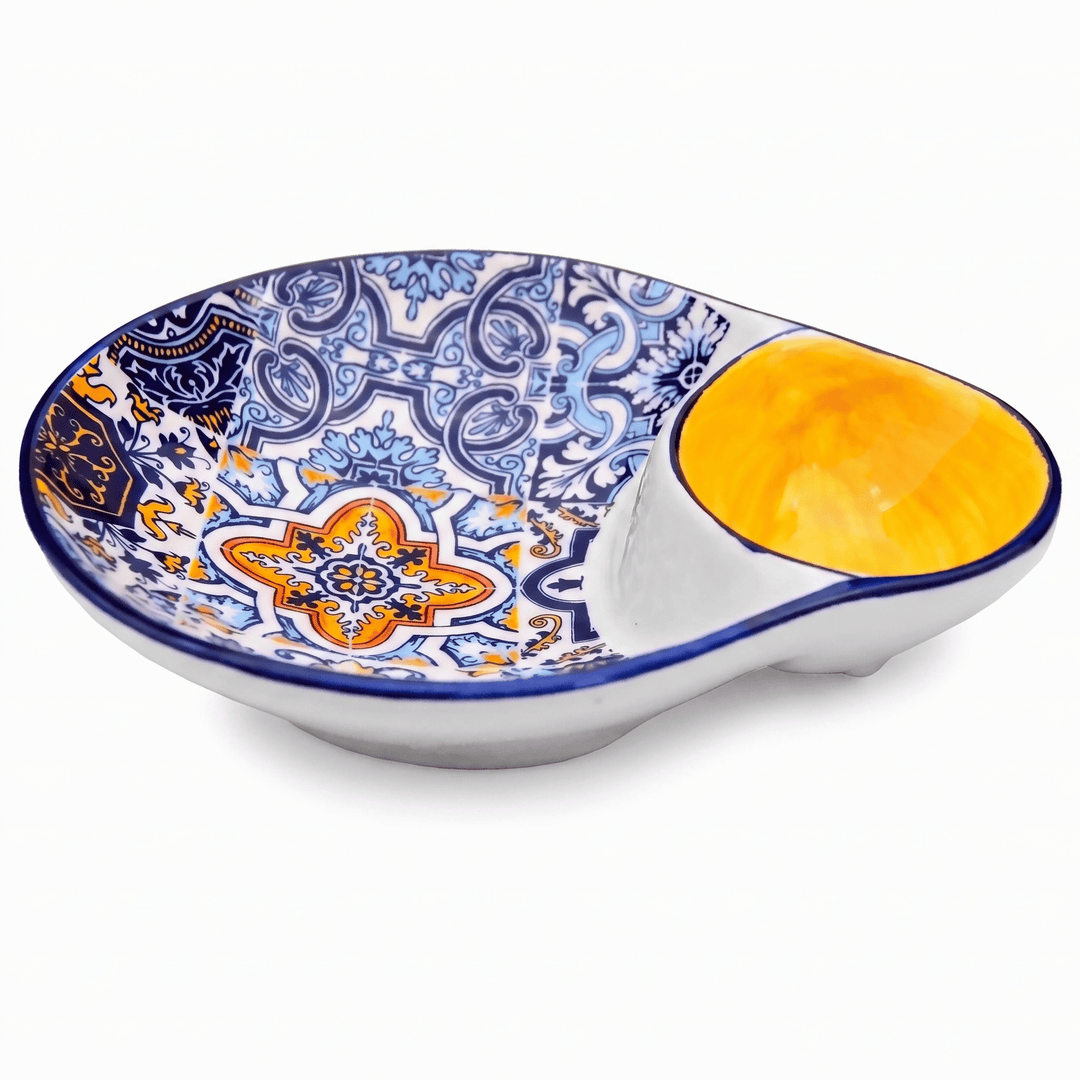 A ceramic Spanish-style dip bowl with a white base, blue and orange floral patterns on the interior, and a glossy yellow-orange glazed recess for the dip, shown on a white background.