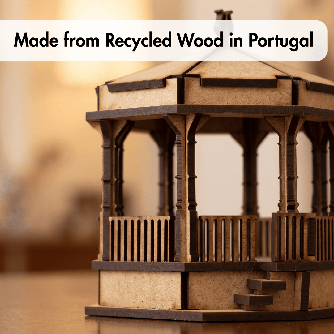 A small wooden gazebo or pavilion model made from recycled wood, shown on a tabletop with a warm blurred background. A white text banner at the top reads &