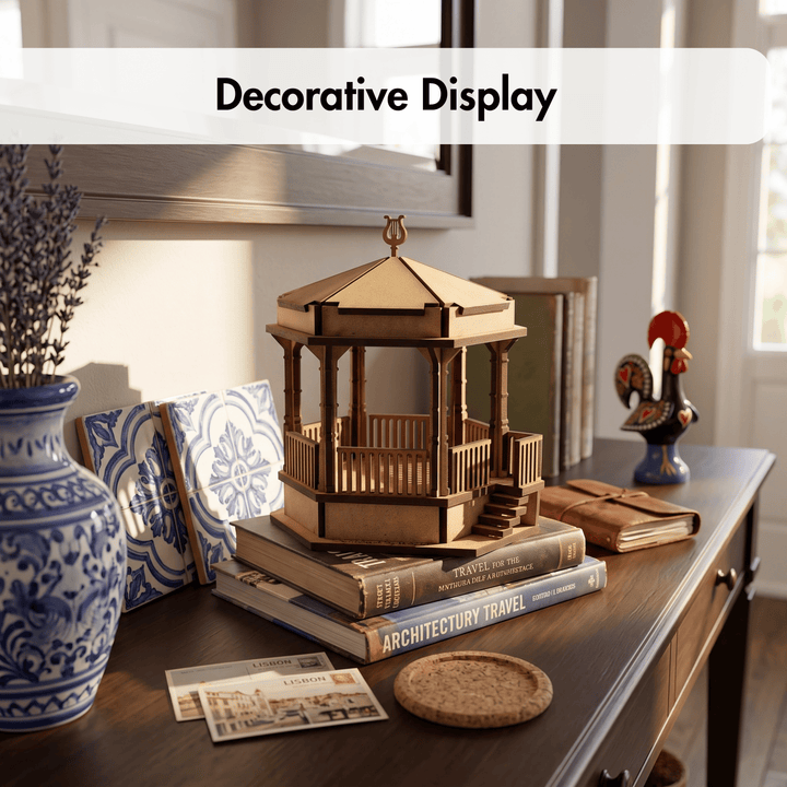 A wooden gazebo model displayed on books on a wooden console table, with a blue-and-white ceramic vase, patterned coasters, and other home decor in a styled interior setting. A white banner at the top reads &