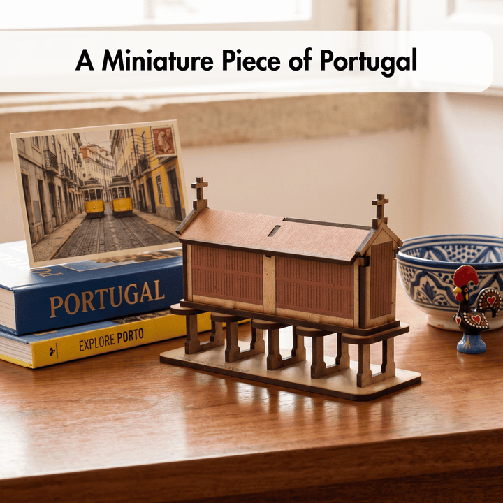 A miniature wooden model of a Portuguese church on a raised platform, displayed on a wooden table next to a book, a postcard, and a decorative bowl. A text banner at the top reads &