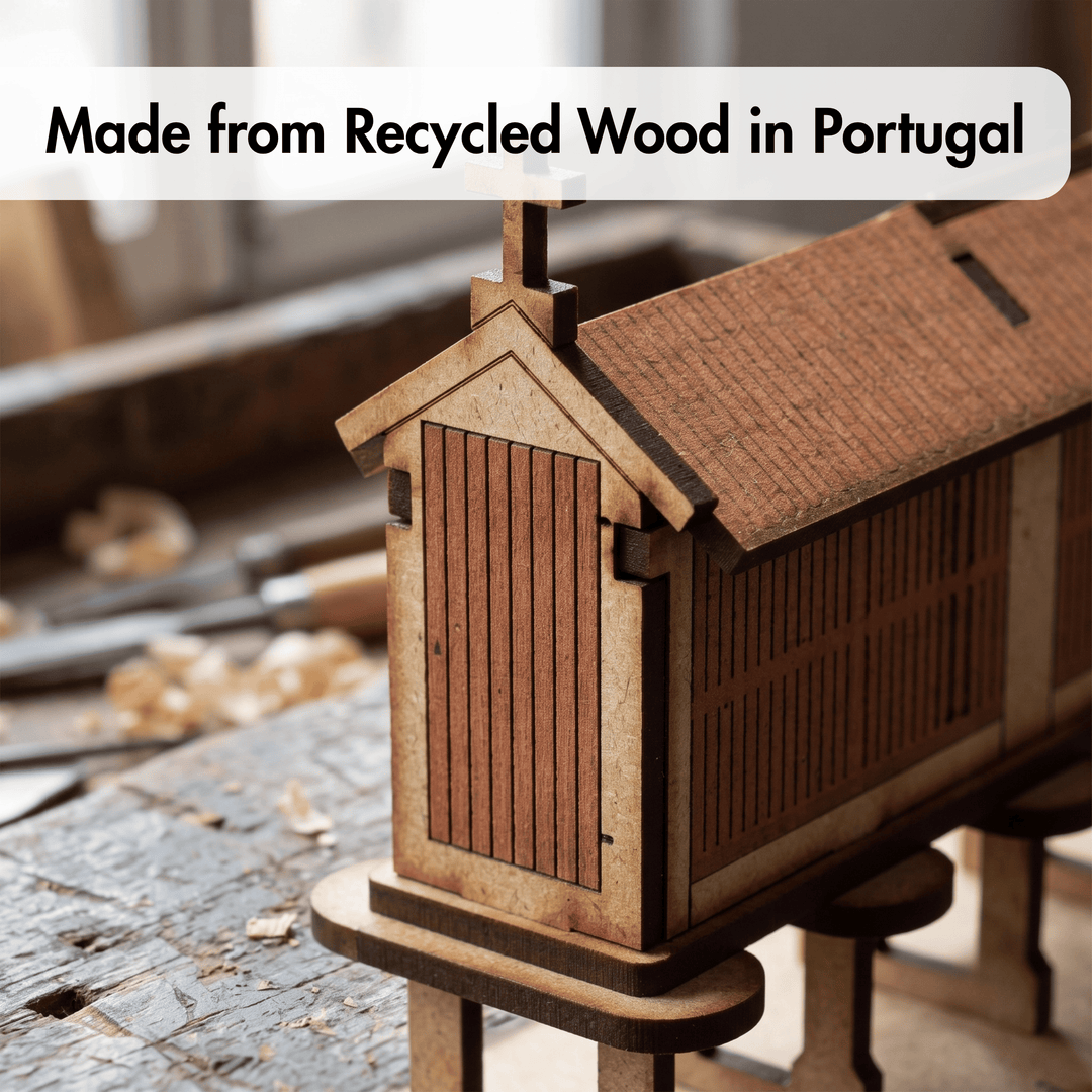 A small wooden house model or miniature cabin made from recycled wood, shown on a workbench with blurred workshop tools in the background. A text banner at the top reads &