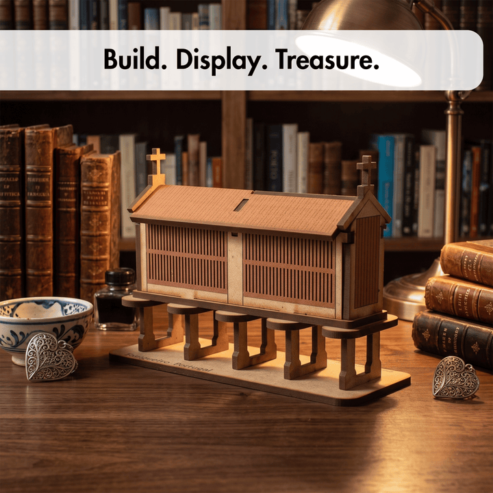 A wooden miniature church model displayed on a wooden table in a warm, book-filled room setting. The church features a pitched roof, small wooden pews in front, and a base with a cross on each end.