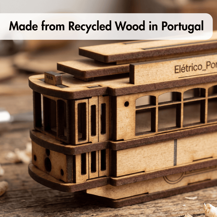 A close-up of a laser-cut wooden trolley model with visible wood grain, shown on a rustic wooden surface. A text banner at the top reads &