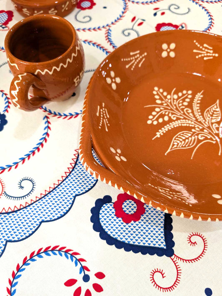 Ceramic plate and cup with floral design on a patterned tablecloth