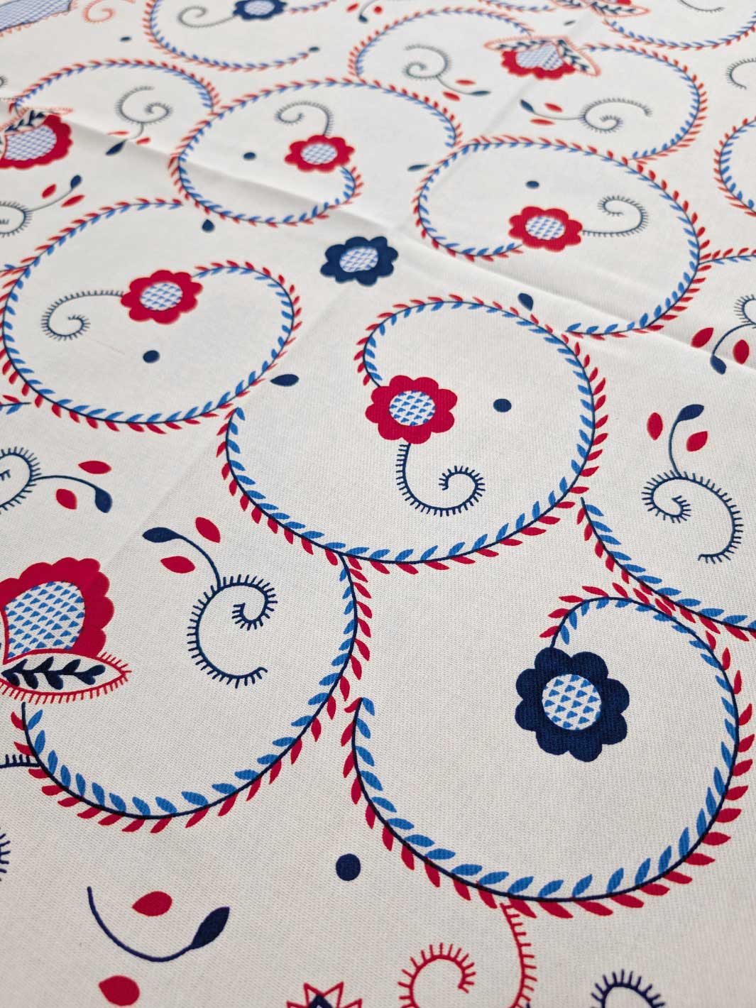 Close-up of fabric with red, blue, and white floral and circular patterns on a beige background.