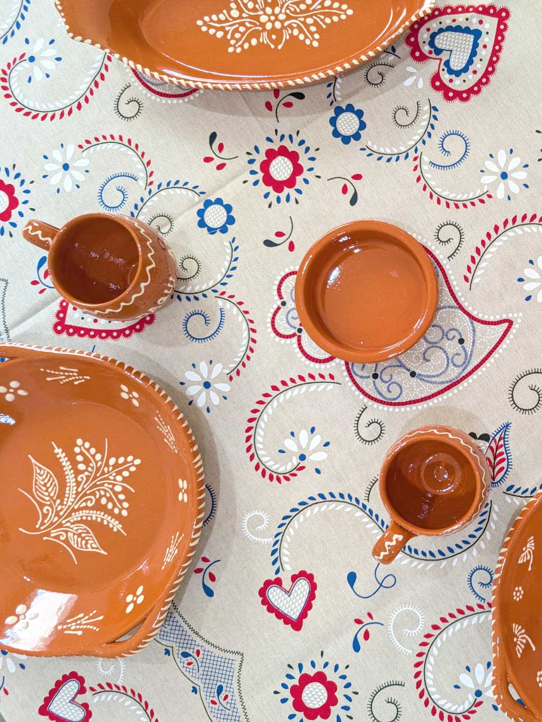 Ceramic plates and cups with floral patterns on a decorative tablecloth.