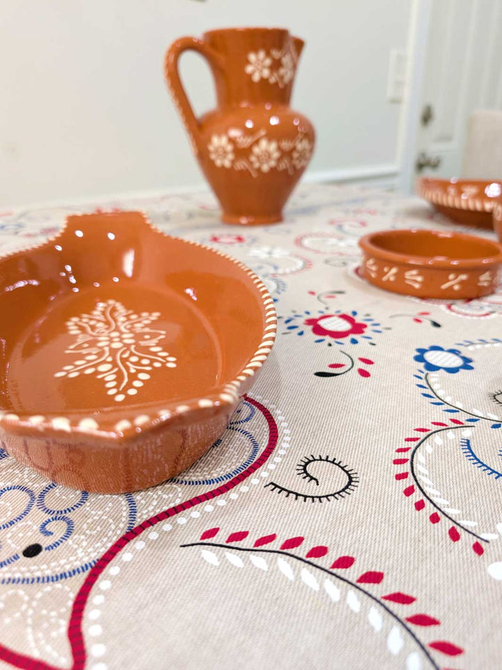 Ceramic bowls and a pitcher on a decorative tablecloth with floral patterns.