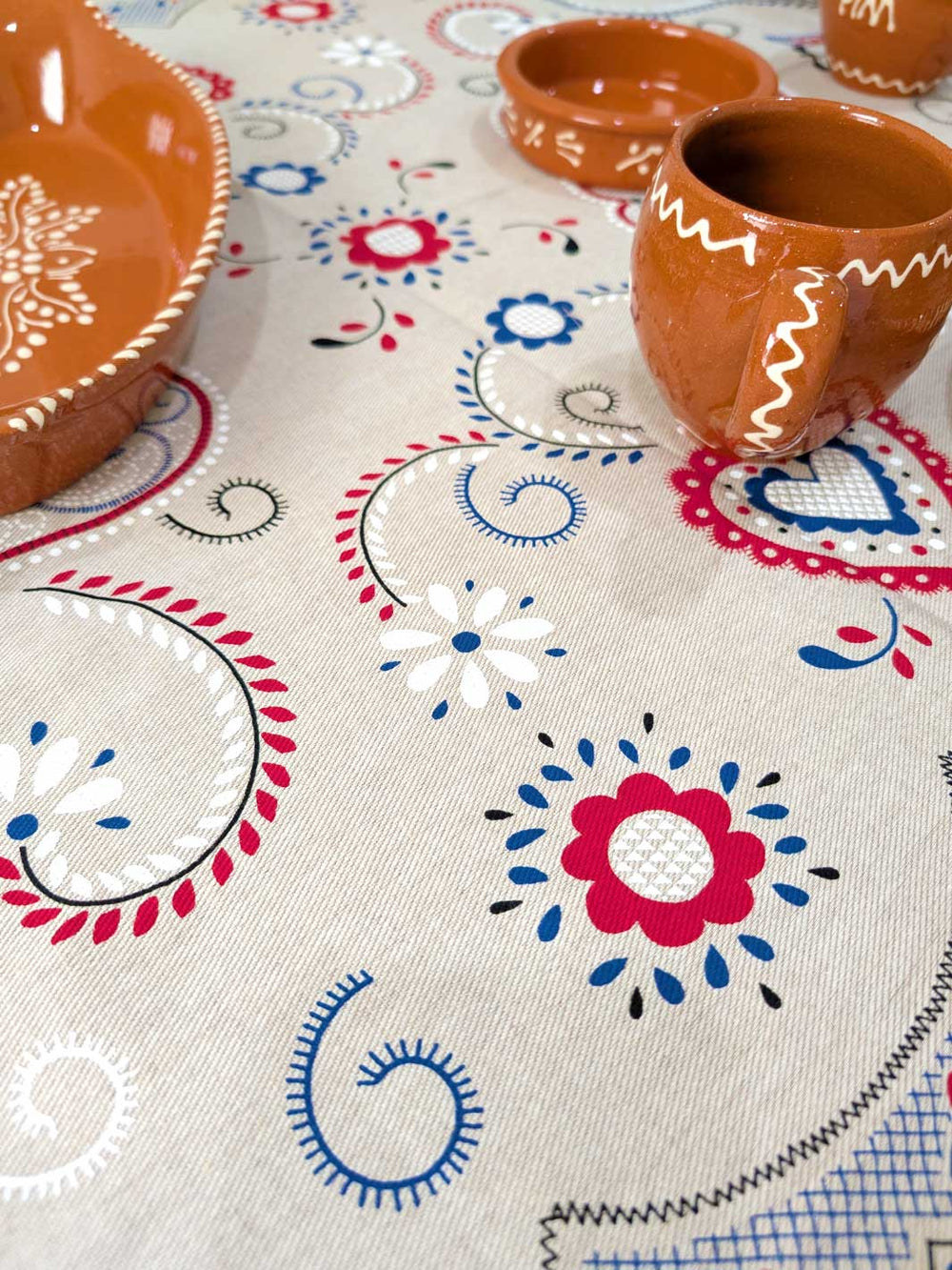 Decorative tablecloth with floral patterns and terracotta bowls on a white background