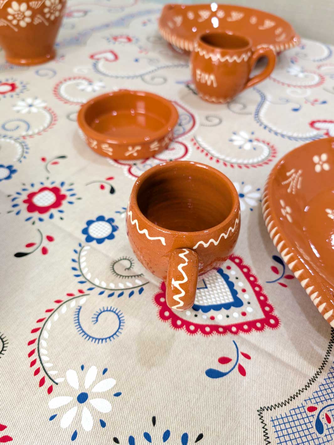 Set of terracotta mugs and bowls on a patterned tablecloth
