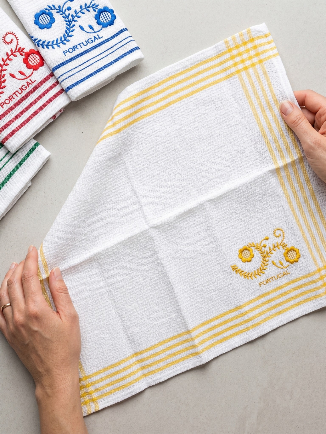 White towel with yellow stripes and embroidered design held by a hand on a light gray surface.
