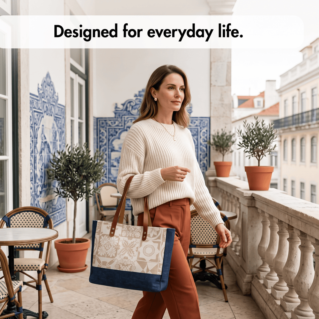 A woman walks on a balcony carrying a large tote bag. The bag has a cream and white geometric pattern on the front, a navy blue bottom panel, and brown shoulder straps.